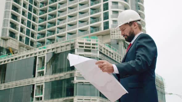 Engineer Male in a White Safety Helmet Developer at a Construction Site Checks on the Drawings at