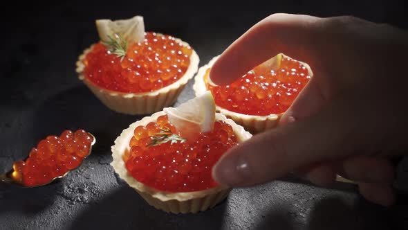 Red Caviar Served in Tartlets on a Black Background. Woman Takes One Tartlet with Caviar
