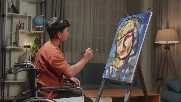 Asian Artist Boy In Wheelchair Holding Paintbrush And Painting A Girl's Face On The Canvas