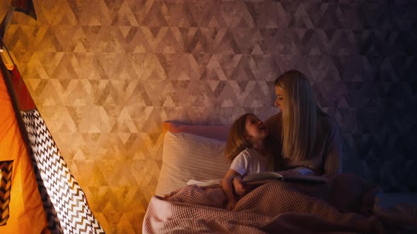 Little Girl and Mum with Book on Bed at Illuminated Wigwam