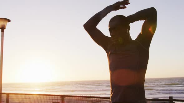 Focused african american man stretching, exercising outdoors by seaside at sunset