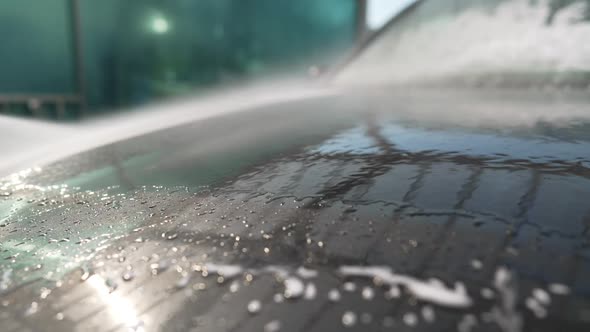 Car Wash Shampoo Washing Off with High Pressure Water From Hood Outdoors in Sunbeam