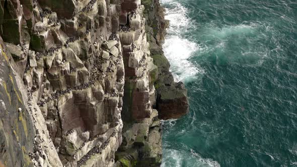 A slow tilting shot rising from a turquoise blue ocean as waves crash against the base of a seacliff