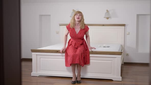 Relaxed Excited Caucasian Transgender Woman in Dress and Shoes Falling Back on Soft Cozy Bed at Home