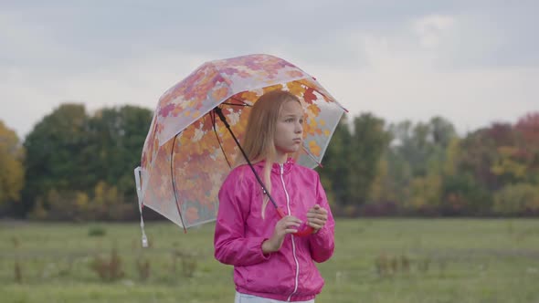 Sad Caucasian Blonde Girl Dressed in Pink Jacket Holding Collorful Umbrella with Painted Yellow