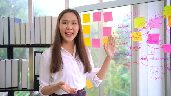 Young Creative businesswoman holding a marker and writing plan and share idea on glass wall with sti