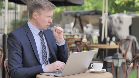 Coughing Businessman Working on Laptop in Outdoor Cafe