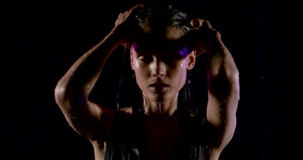 Portrait of a Beautiful Wet Girl Standing on a Black Background in Heavy Rain, She Runs Her Hands