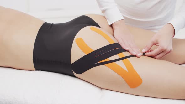 Therapist is applying kinesio tape to female body. Physiotherapy, kinesiology and recovery.