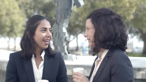 Brunette Businesswomen Drinking Coffee Outdoors and Talking