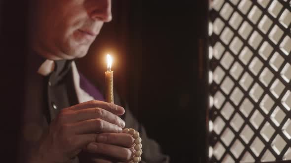Priest Blowing Out Candle in Confession Booth
