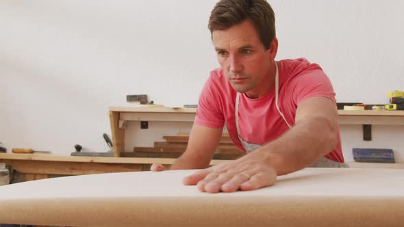 Caucasian male surfboard maker checking a wooden surfboard before polishing