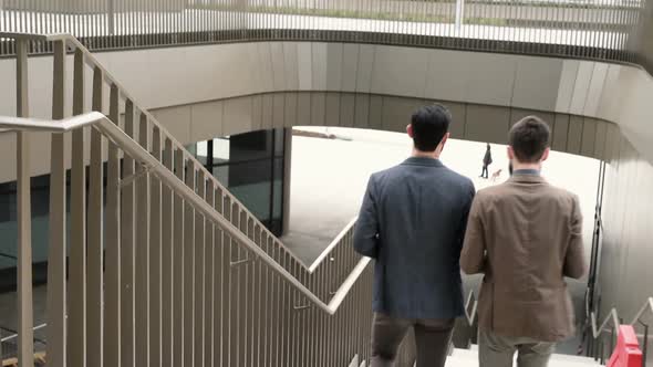 From behind two young bearded business men walking downstairs business district discussing