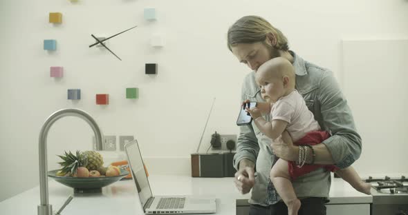 Daughter holding mobile phone while father using laptop