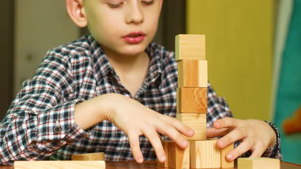 A carefree Caucasian boy of 7-8 years old builds a tower from wooden blocks while at home