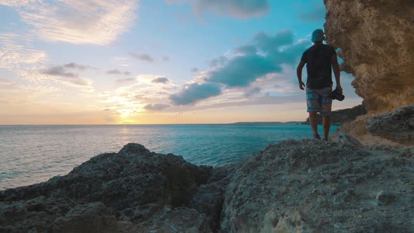 Young boy with photo camera walking along cliff side during sunset, Curacao