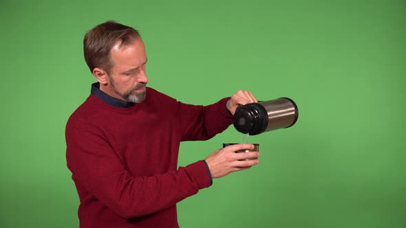 A Middleaged Handsome Caucasian Man Drinks From a Vacuum Bottle  Green Screen Background