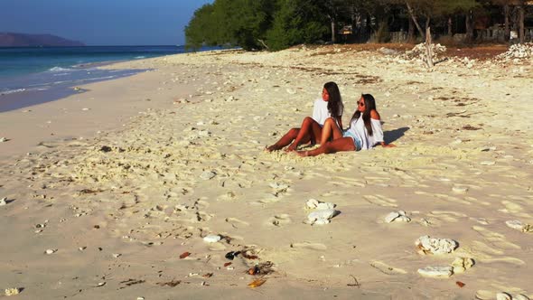 Girls relaxing on tranquil lagoon beach voyage by blue sea and bright sandy background of Bali after