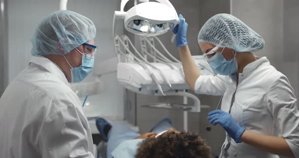 Dentist and Assistant Adjusting Lamp Over Patient Sitting in Chair