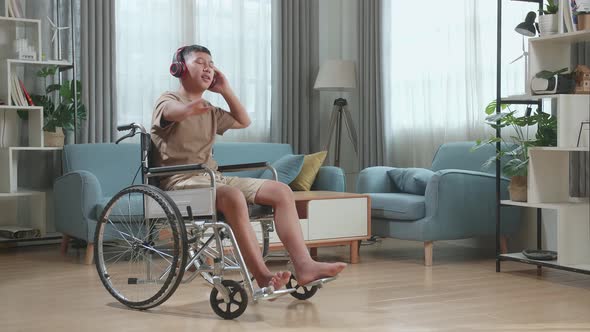 Asian Boy Sitting In A Wheelchair Listening To Music With Headphones And Dancing In Living Room