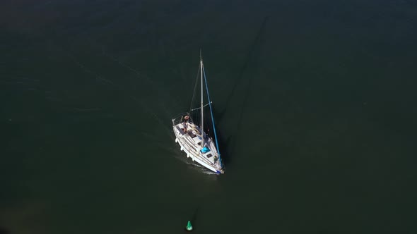 Sailing yacht with long shadow navigates on her motor along the green buoy over the clear green wate