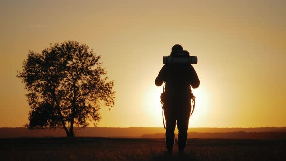 Silhouette of a Man with a Backpack Against Bright Sky Sunset. Sun Goes Down. Travel Concept. Slow