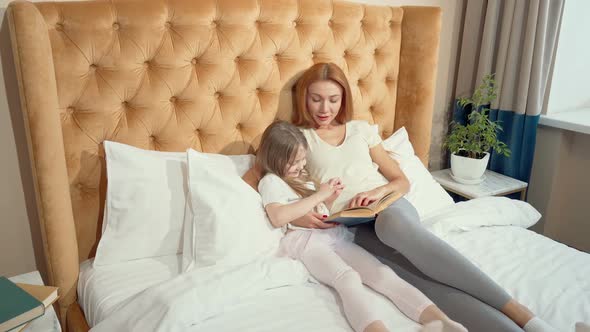 Top View Shot of a Mother and Daughter Reading a Book Lying in Bed