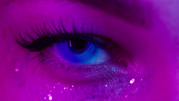 Closeup of Young Woman Eye Wearing Decorative Lenses in Ultraviolet Light Makeup with Glitter and