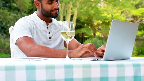 Smiling man using laptop while having wine in garden 4k