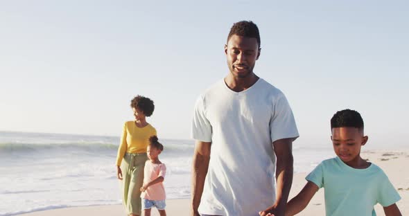 Smiling african american holding hands and walking on sunny beach