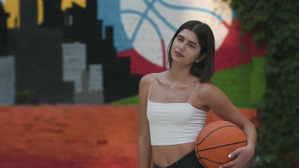 Middle Shot of Confident Young Fit Sportswoman Posing with Ball on Outdoor Court