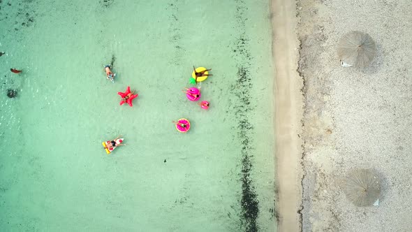 Aerial view of friends floating on inflatable mattresses in transparent sea.