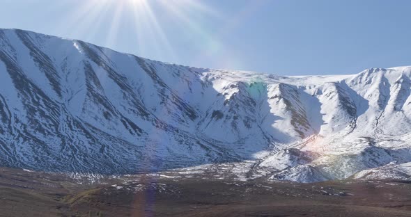 Timelapse of Sun Movement on Crystal Clear Sky Over Snow Mountain Top. Yellow Grass at Autumn Meadow