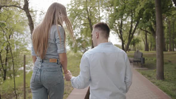 A Young Girl Goes Along the Curb of the Path in the Park and Holds Onto the Arm of Her Beloved Man