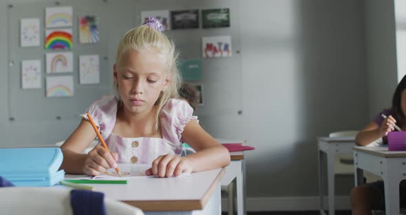 Video of focused caucasian girl sitting at desk in classsroom