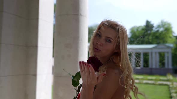 Portrait of a Blonde with Big Breasts in a Red Fluffy Dress and with a Rose