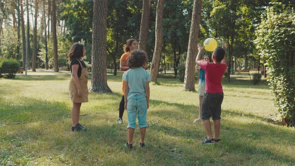School Kids Playing Ball with Young Female Teacher in Public Park