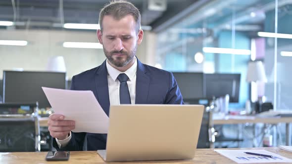 Young Businessman Reading Documents on Office Desk