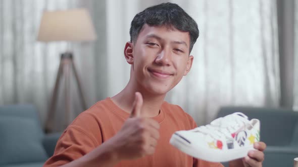 Smiling Asian Boy Footwear Designer Holding Colourful Pattern Sneaker And Showing Thumbs Up Gesture