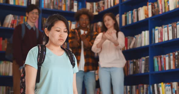 Diverse Students Bullying and Laughing at Sad Asian Young Woman in Library