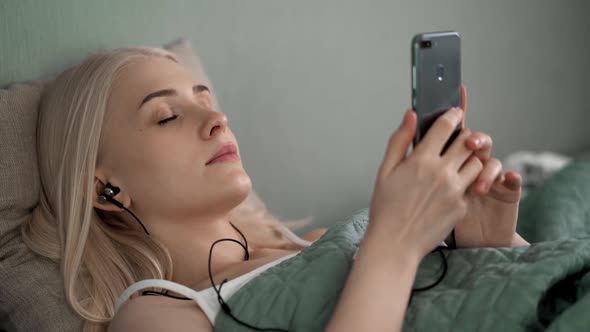 Beautiful Girl Lying on the Bed Listening To Music with Headphones