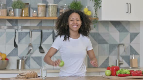 African Woman Showing Thumbs Up While Holding Apple in Kitchen