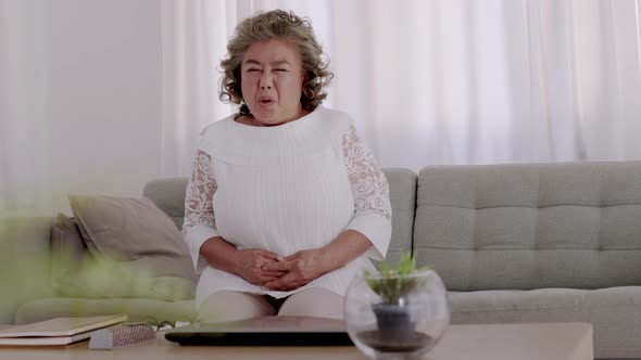 Asian Elderly woman Stomachache on sofa in living room.