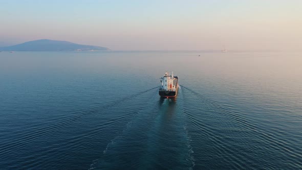 Aerial View Following the Ultra Large Cargo Ship at Sea Leaves Port at Sunset