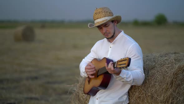 Man Wearing a Straw Hat Playing the Guitar About a Haystack