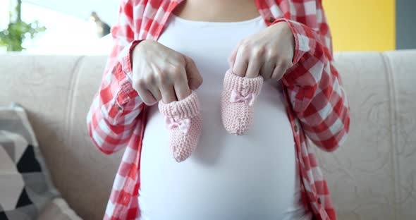 Pregnant Woman Holds Pink Slippers for Newborn Closeup