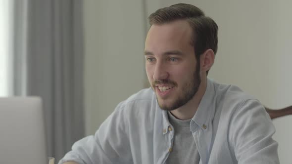 Portrait of a Young Handsome Man Smiling and Nodding Sitting in Front of His Computer in the Office