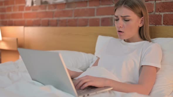 Young Woman Reacting to Loss on Laptop in Bed