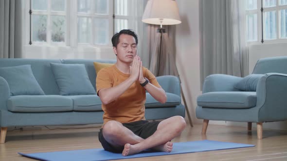 Asian Man Doing Yoga In Sukhasana Pose On Mat At Home