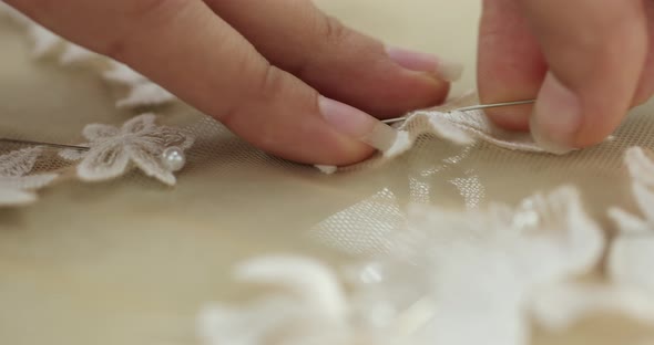 seamstress's hands fasten a pin into the white fabric pattern of a part of a wedding dress